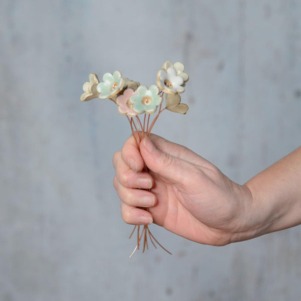 hand holding bunch of ceramic flowers with copper stems