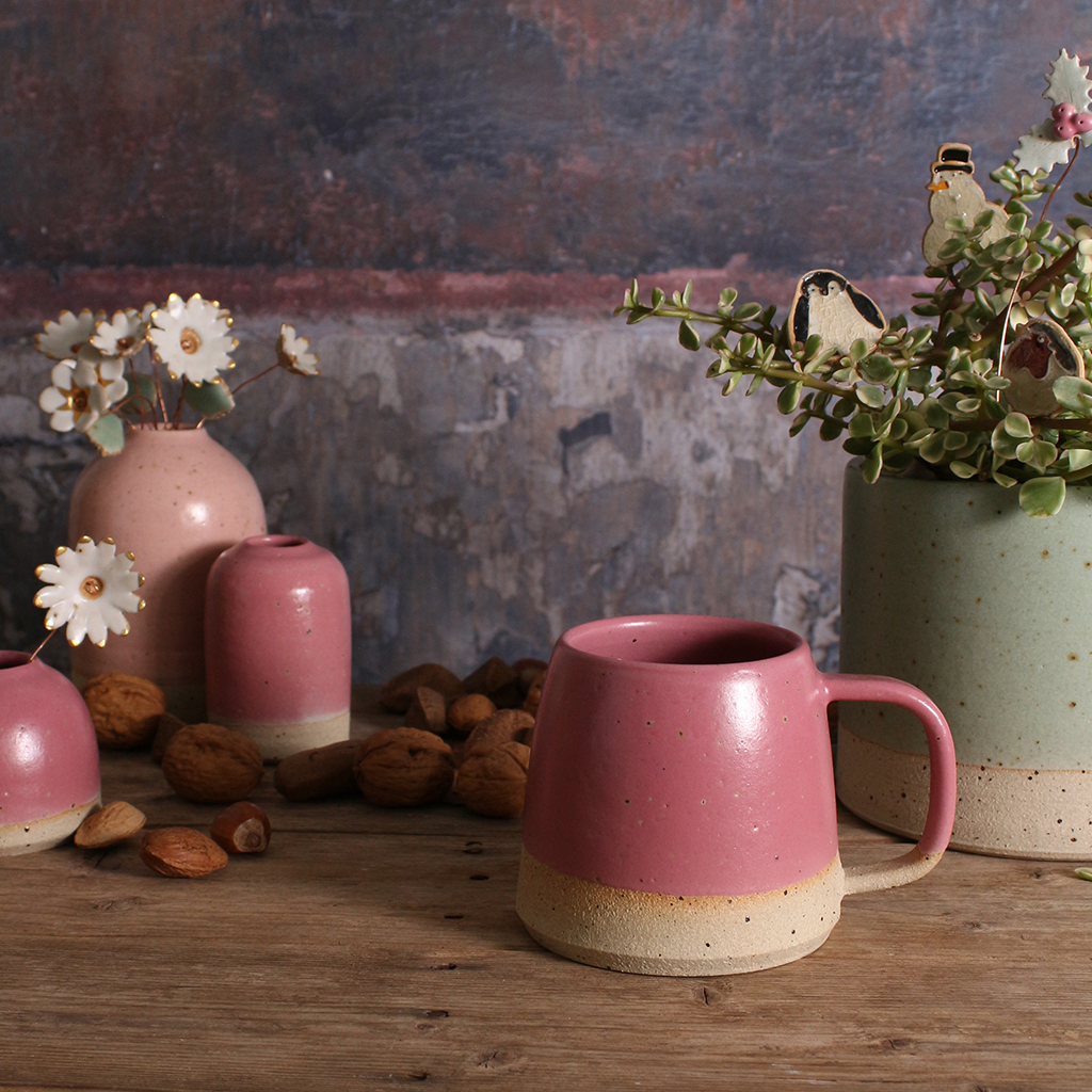 Pink ceramic mug and vases on a wooden surface with a rustic background