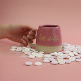 Pink mug with 'hot stuff' text held by a hand, surrounded by candy love heart sweets on a pink background