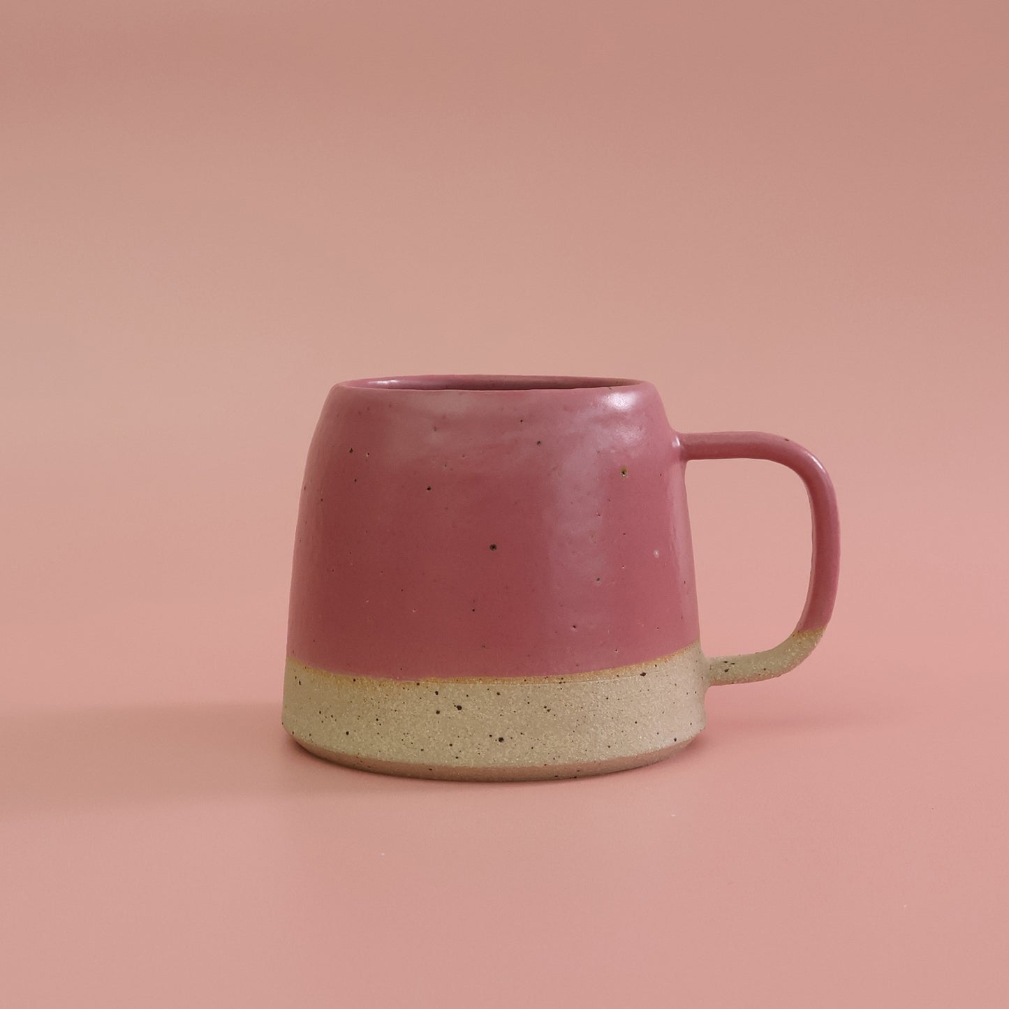 Pink ceramic mug with a beige base on a pink background