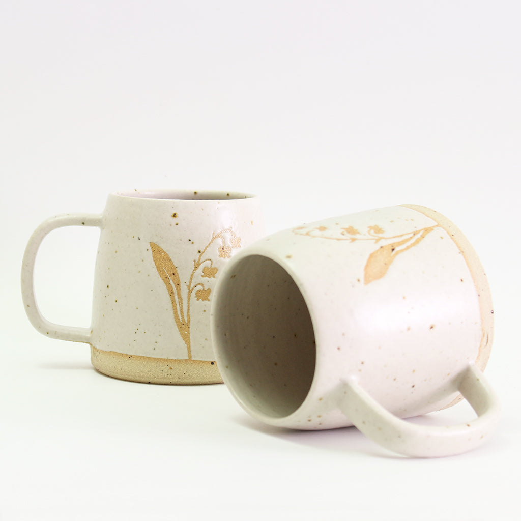 Two Lily of the Valley mugs, one on its side