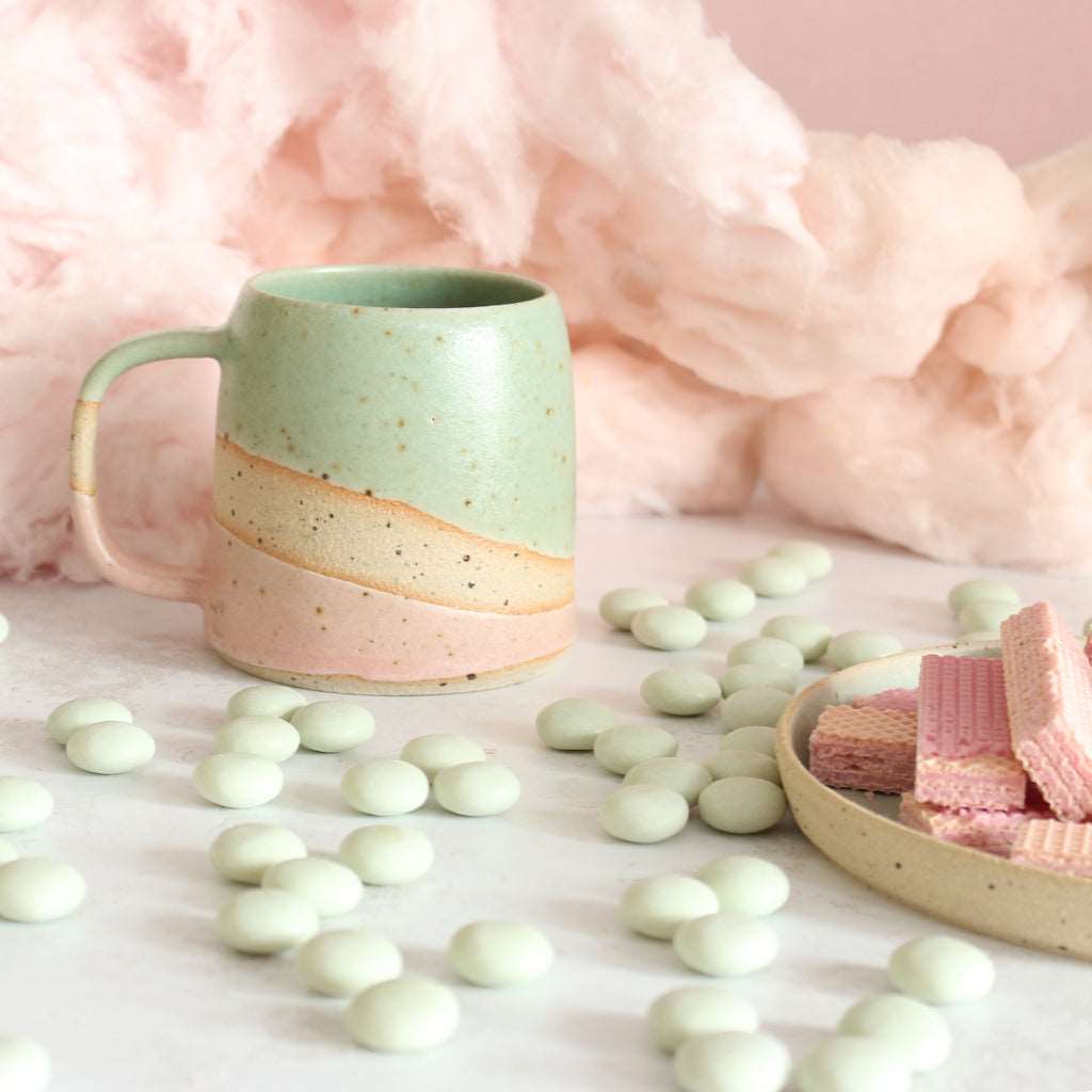 Green and pink stoneware mug next to mints and wafers.