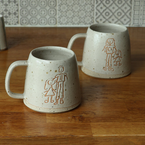 Two ceramic mugs with engraved figures on a wooden surface.