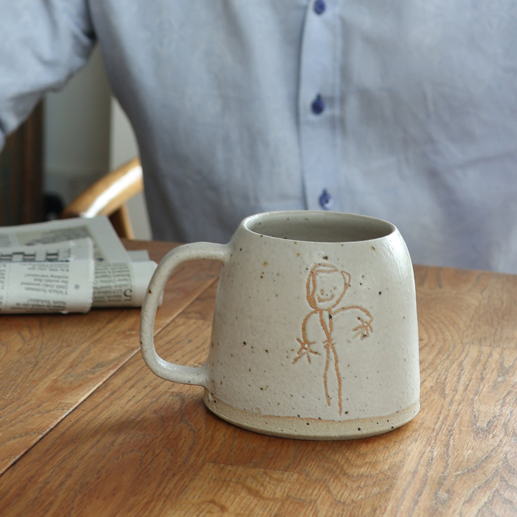 handmade stoneware mug with children's drawing on it. Mug is on a wooden table