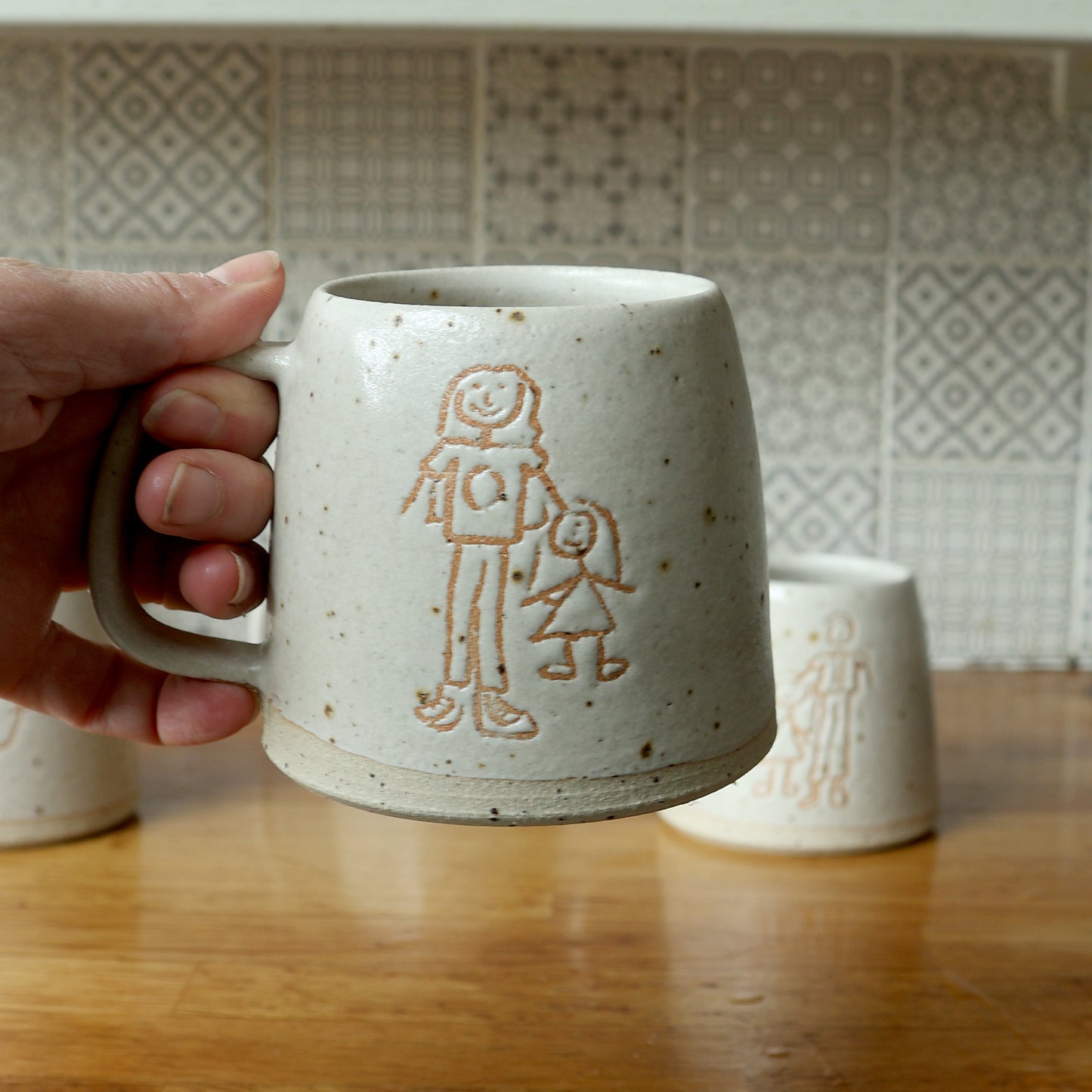 Hand holding a custom Children's drawing mug glazed in white glaze. The mug features a drawing of a mum with her child