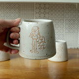 Hand holding a custom Children's drawing mug glazed in white glaze. The mug features a drawing of a mum with her child