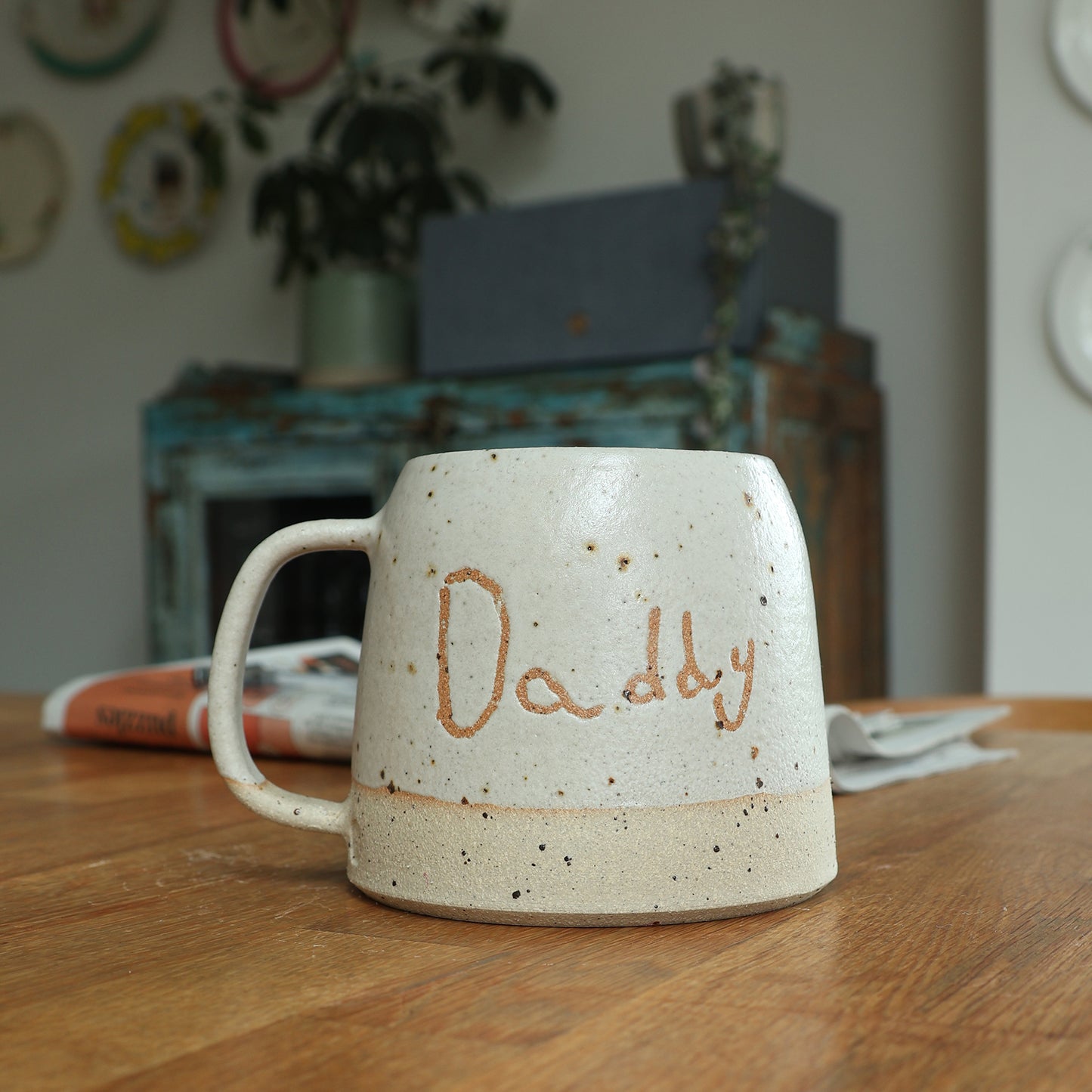 Custom handwriting ceramic mug with the name 'Daddy' on a wooden table with a newspaper in the background. 