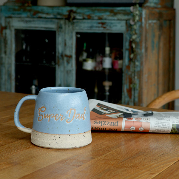 Handmade ceramic mug personalised with the words super dad. the mug is on a wooden table