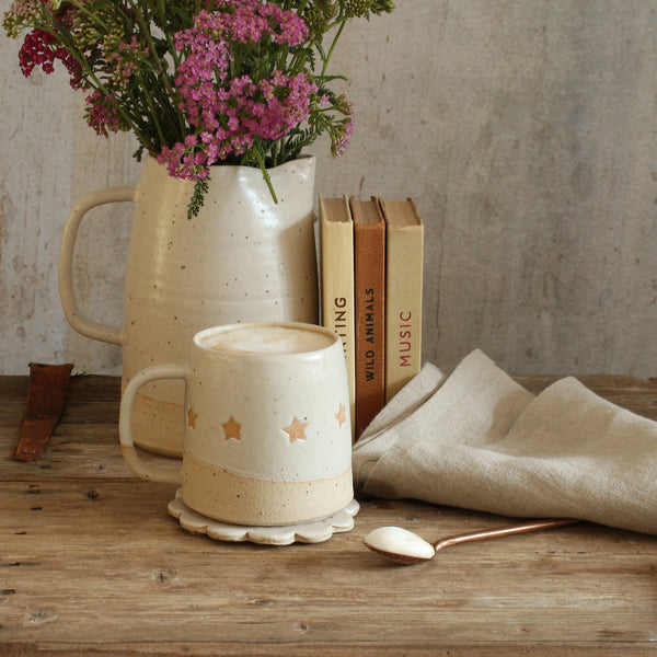 Star mug in front of stack of old books and pitcher of wildflowers