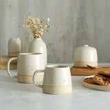 Habulous small stoneware mug off-white in front of large white mug and table setting of white stoneware ceramics