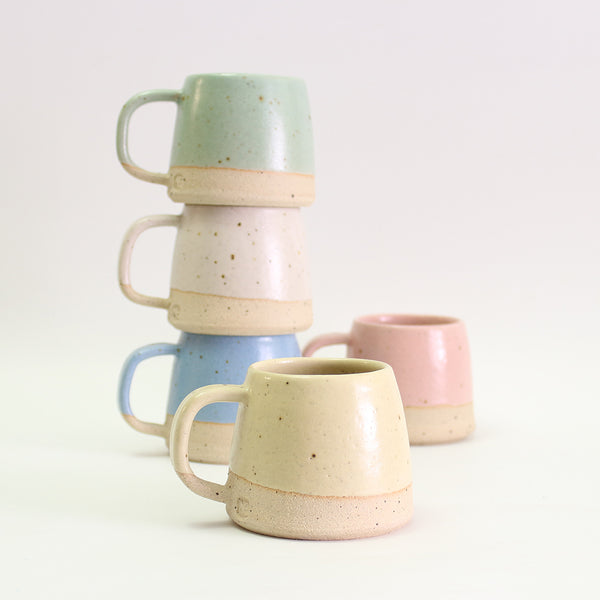 Small light yellow mug in front of stack of pastel small mugs