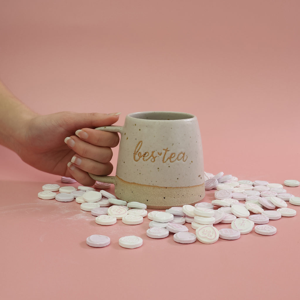 Ceramic mug with 'bestea' text held by a hand on a pink background with tea bags. The mug is handmade by Habulous Ceramics in a British flecked stoneware clay.