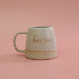 Speckled ceramic mug with 'bestea' text on a pink background
