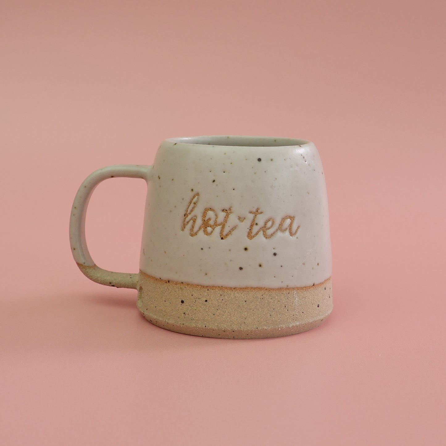 White ceramic mug handmade with fleck clay with 'hot tea' text on a pink background. a pun on the saying Hottie
