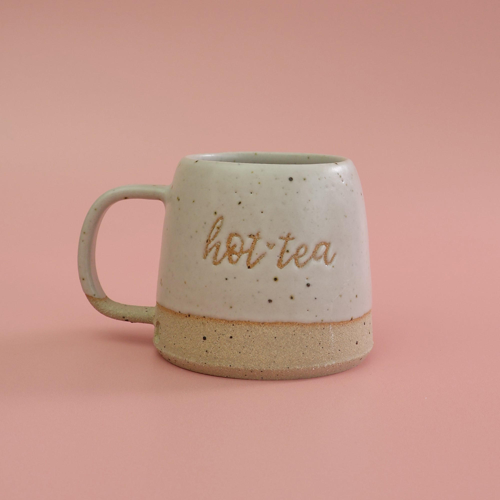 White ceramic mug handmade with fleck clay with 'hot tea' text on a pink background. a pun on the saying Hottie
