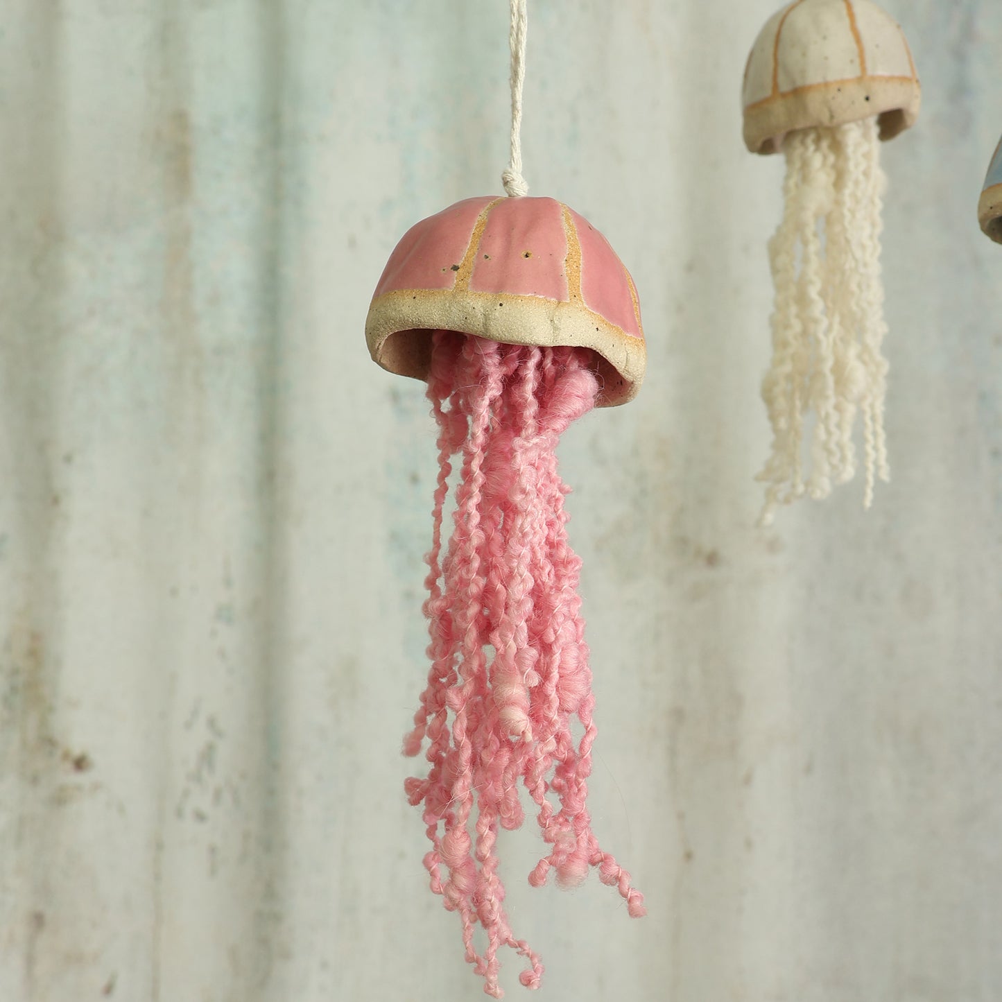 Decorative jellyfish ornamental hanging with pink curly wool tentacles in front of  a textured wall background - handmade by Habulous