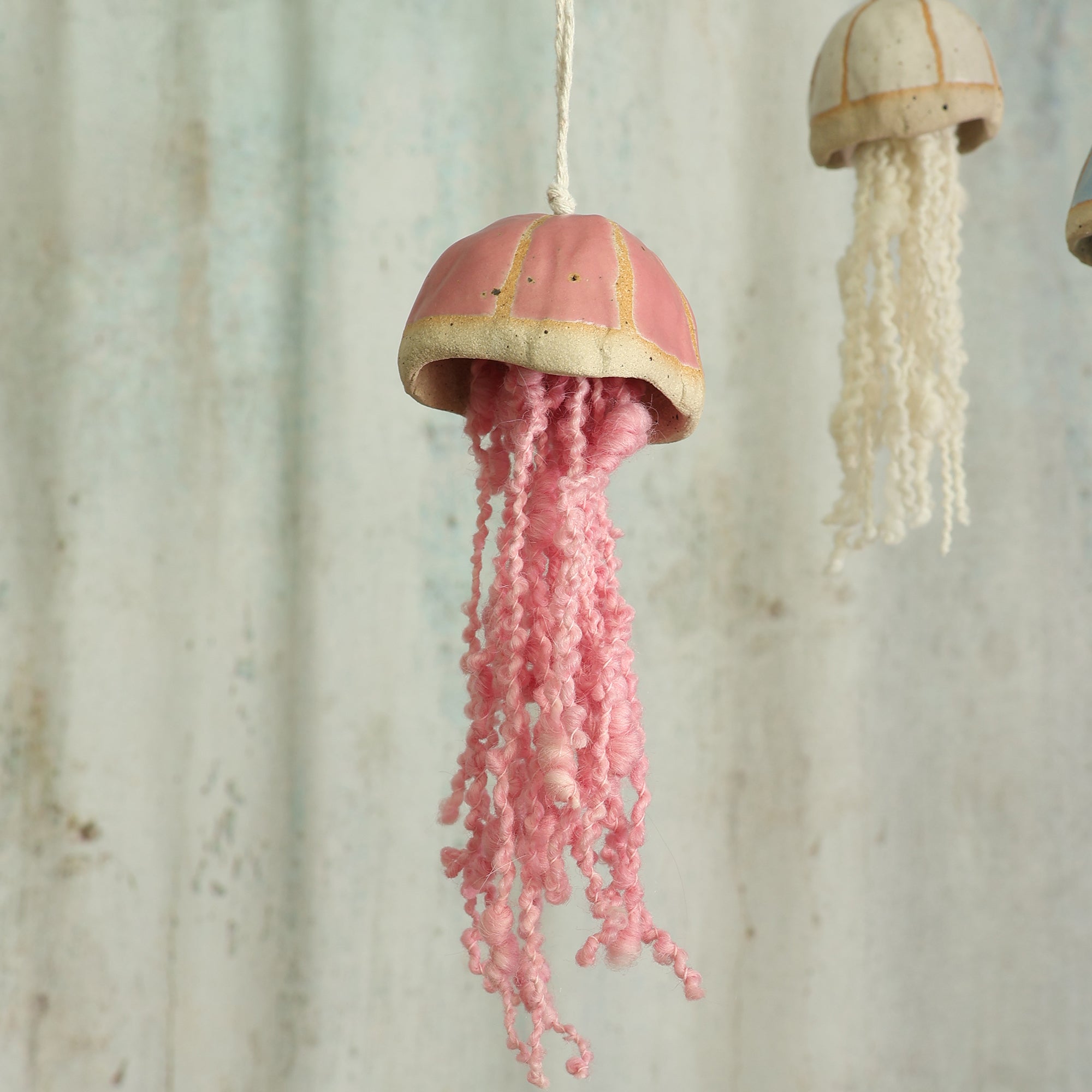 Decorative jellyfish ornamental hanging with pink curly wool tentacles in front of  a textured wall background - handmade by Habulous
