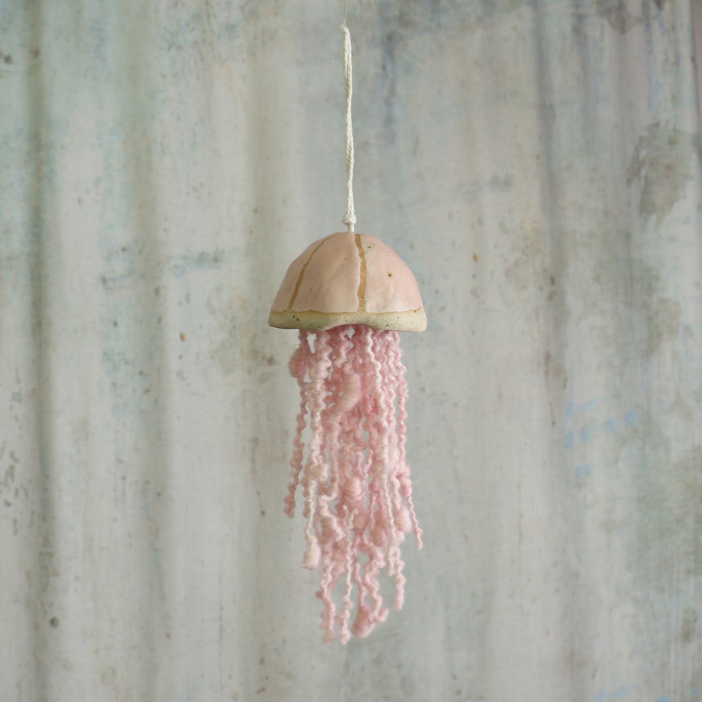 Decorative hanging jellyfish with pink wool tentacles against a rustic grey background - the jellyfish is a handmade ceramic hanging decoration by Habulous Ceramics 