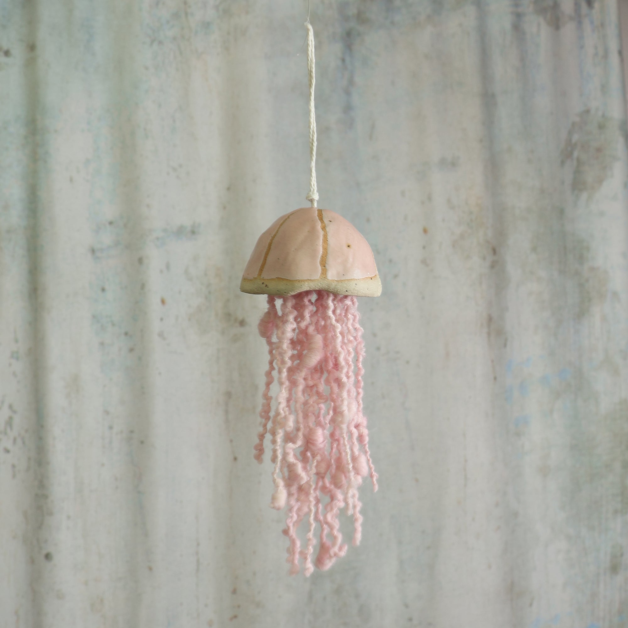 Decorative hanging jellyfish with pink wool tentacles against a rustic grey background - the jellyfish is a handmade ceramic hanging decoration by Habulous Ceramics 