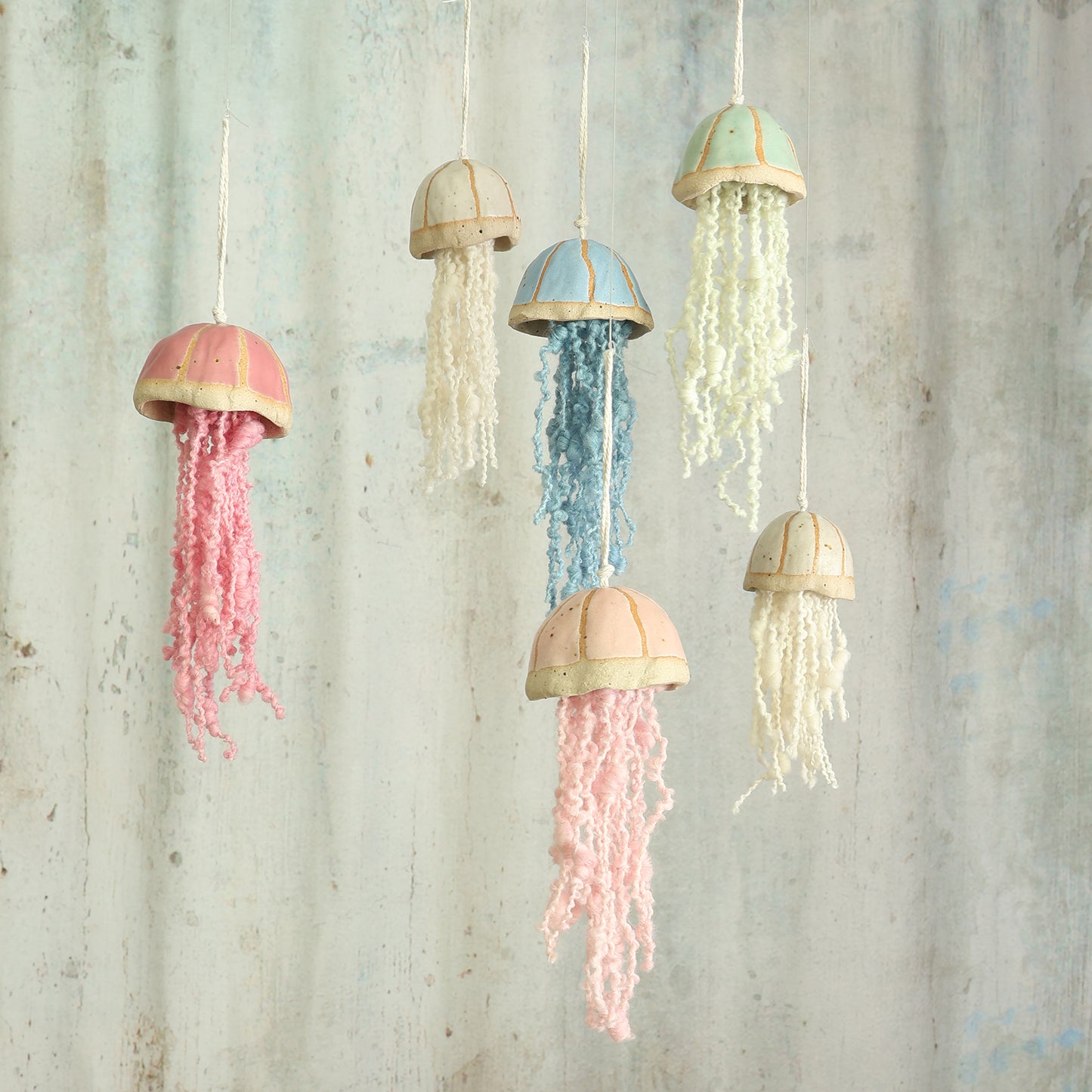 cluster of 6 ceramic jellyfish in blue, green, pink, a pale pink and white hang in front of a textured grey background  the jellyfish are handmade in the UK by Habulous Ceramics 