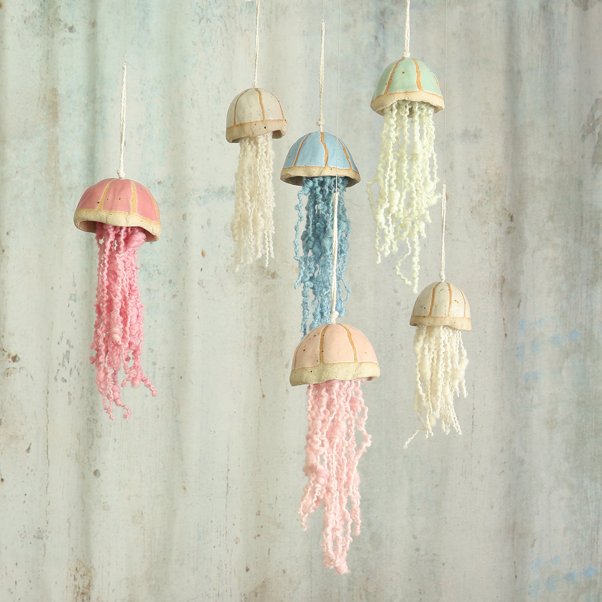 cluster of 6 ceramic jellyfish in blue, green, pink, a pale pink and white hang in front of a textured grey background  the jellyfish are handmade in the UK by Habulous Ceramics 