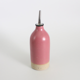 Pink ceramic oil pourer bottle with a metal nozzle on a white background