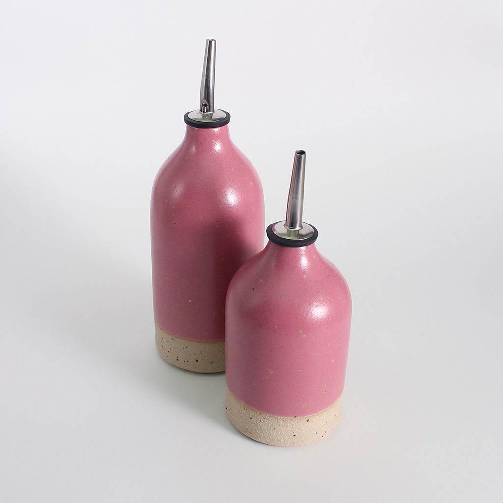 Two pink ceramic oil pouring bottles with metal nozzles on a light grey background