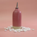 Bright pink handnmade stoneware oil pourer, surrounded by love heart sweets on a lighter pink background 