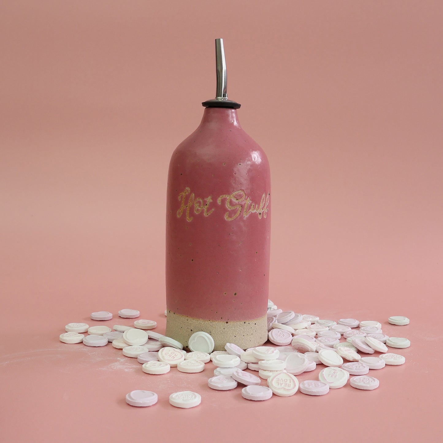 Pink bottle labeled 'Hot Stuff' with love heart sweets and on a pink background
