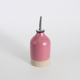 Pink ceramic oil pourer bottle with a metal nozzle on a white background