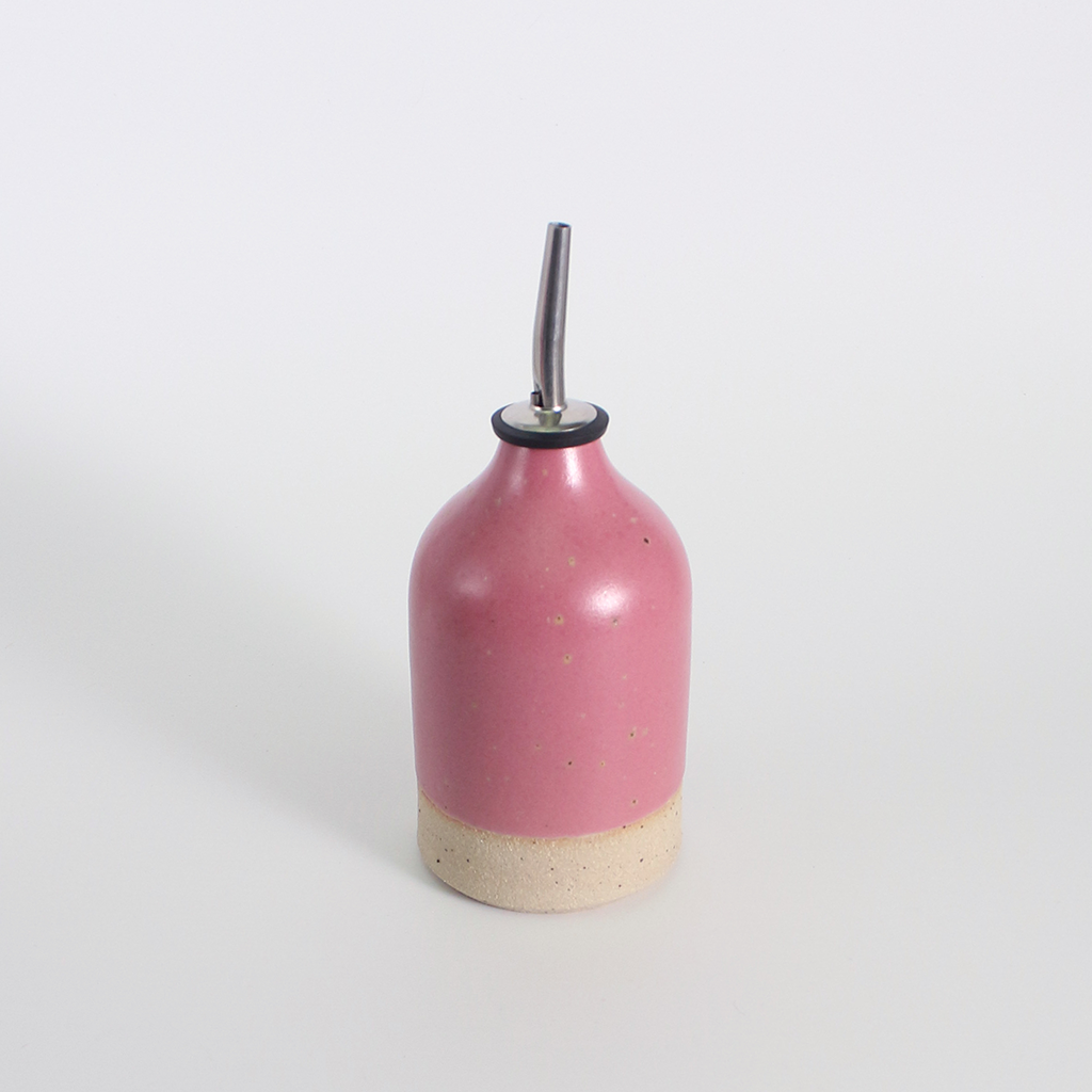 Pink ceramic oil pourer bottle with a metal nozzle on a white background
