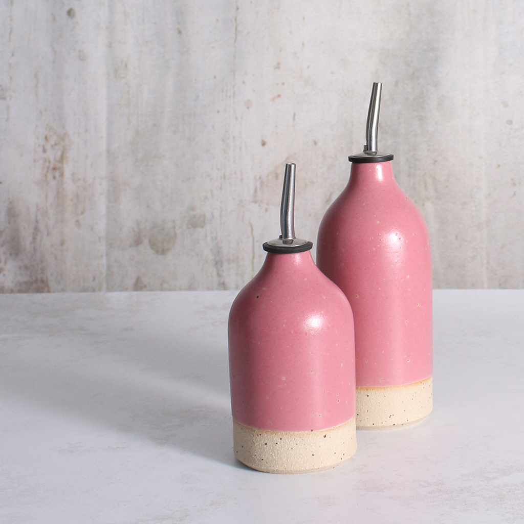two fuchsia pink ceramic oil pourers in various sizes on a white table