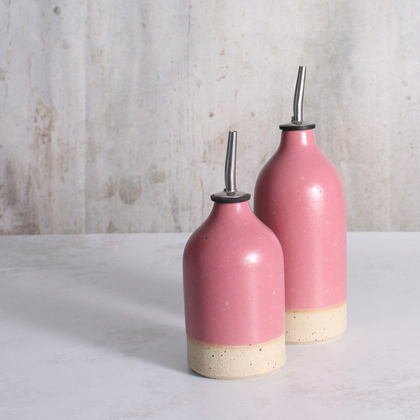 two fuchsia pink ceramic oil pourers in various sizes on a white table