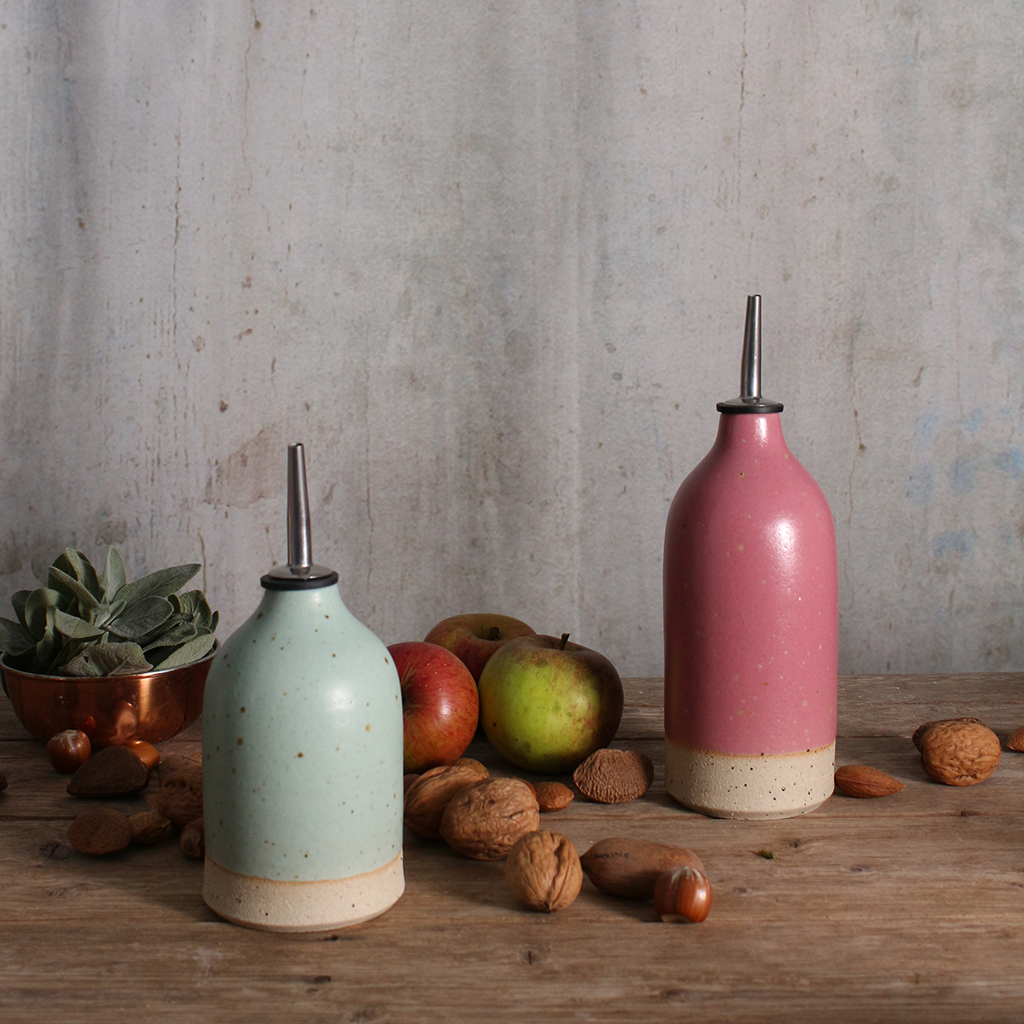 a fuchsia pink and duck egg blue ceramic oil pourers in various sizes on a wooden table surrounded by walnuts and apples
