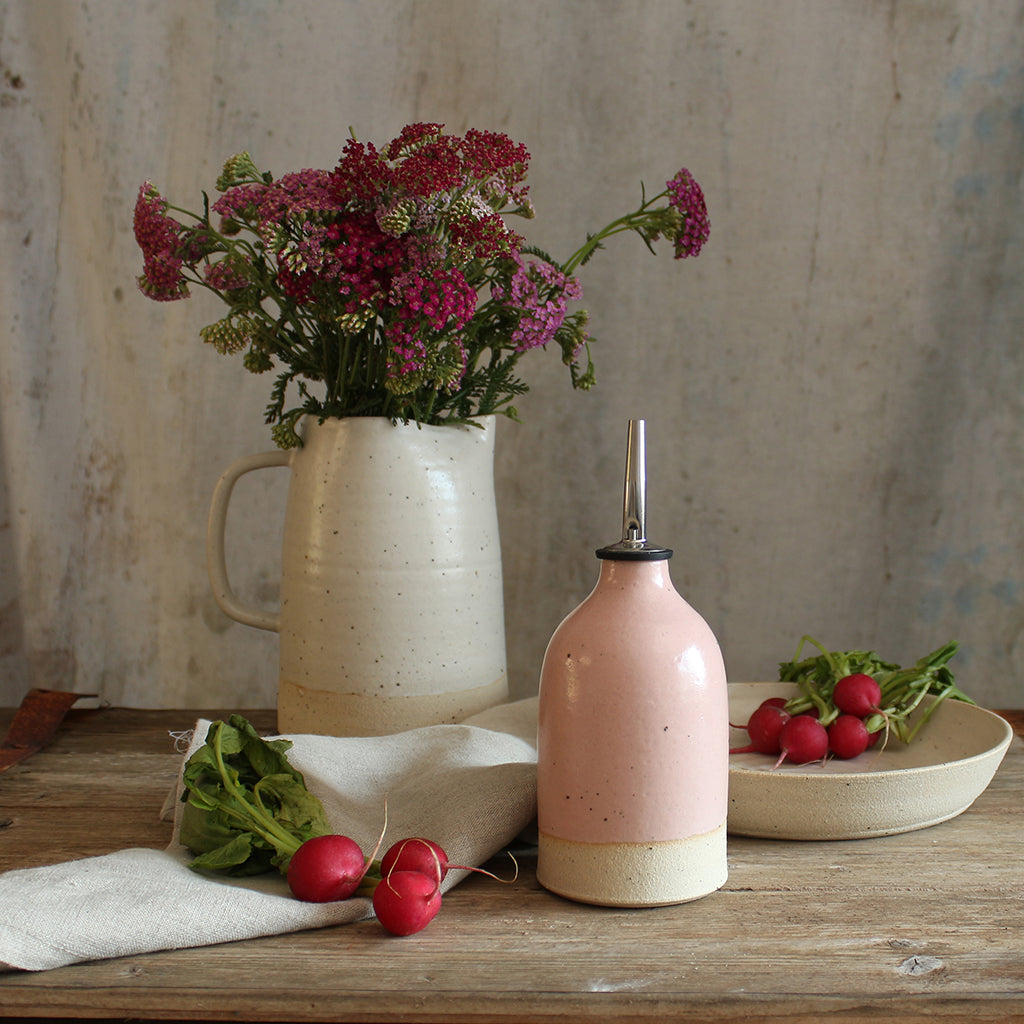 Small pink oil pourer on table with bowl of radishes and jug of wildflowers