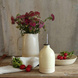 Small yellow oil pourer on table with bowl of radishes and jug of wildflowers