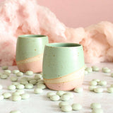 Close up of mint green and pale pink stoneware tumbler with one behind