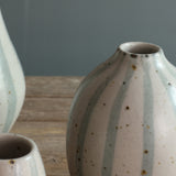 A close-up of a handmade rounded ceramic vase with a blue and white stripe design. 
