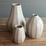 Three handmade ceramic vases in varying heights with vertical blue and white stripes on a rustic wooden table against a panelled wall.