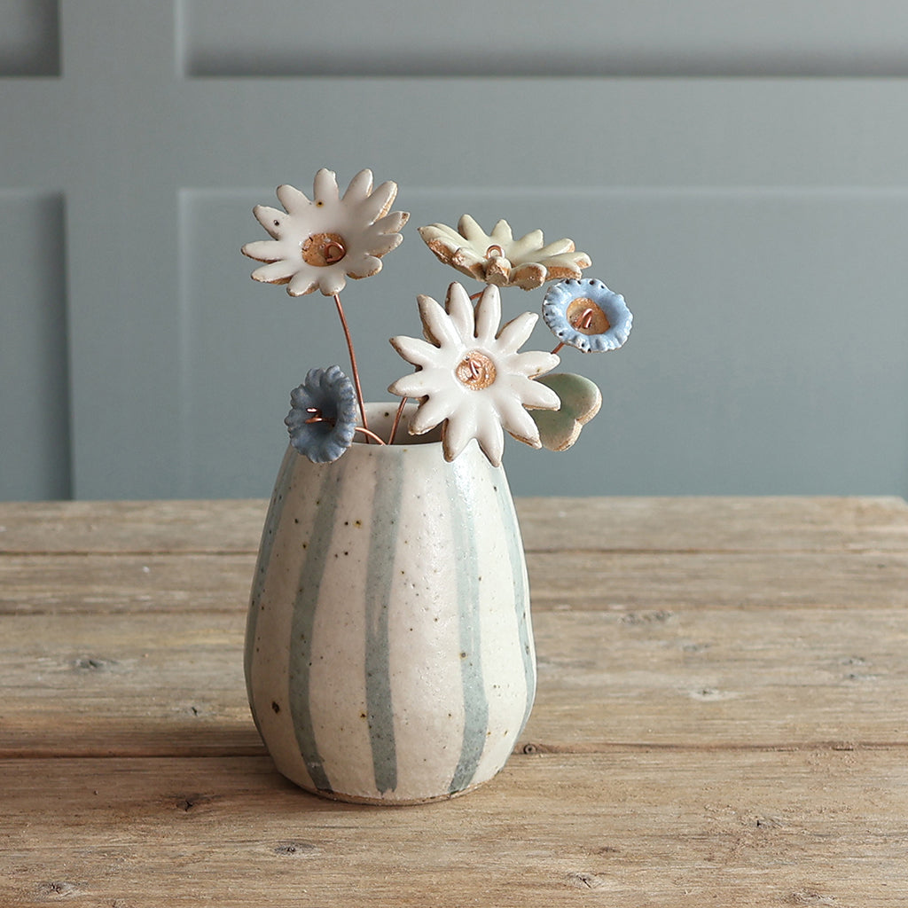 A handmade ceramic vase with vertical blue and white stripes, holding handmade ceramic flowers. 