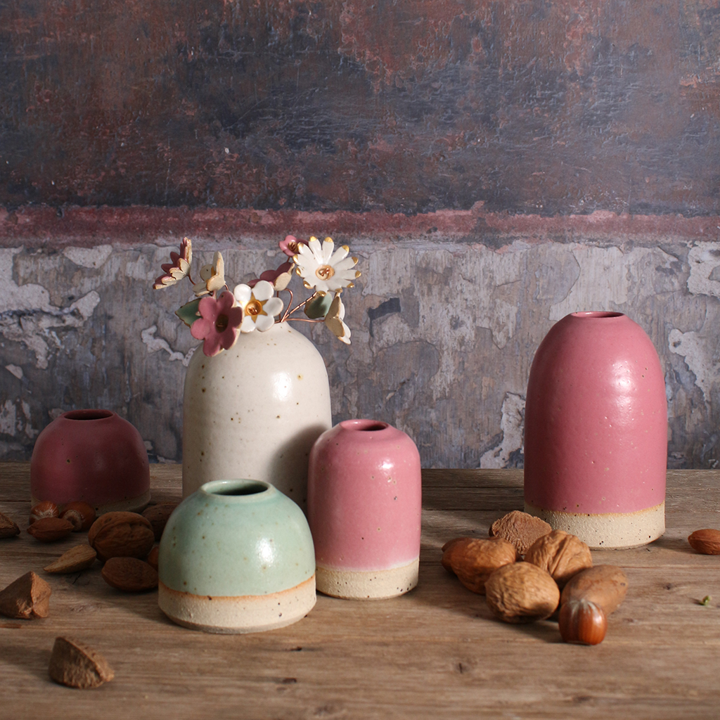 Set of ceramic vases in various colors on a wooden surface with a rustic background.