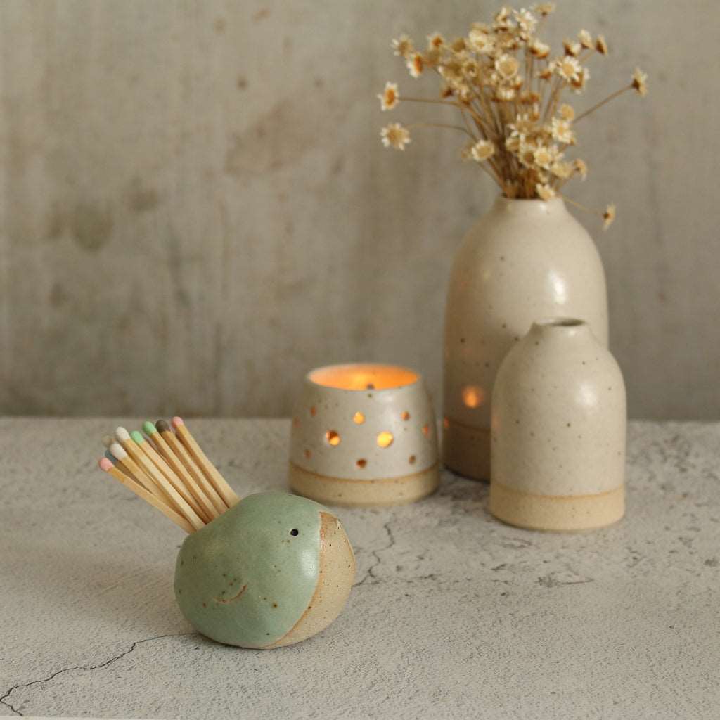 Green bird match pot with matches in front of white vases