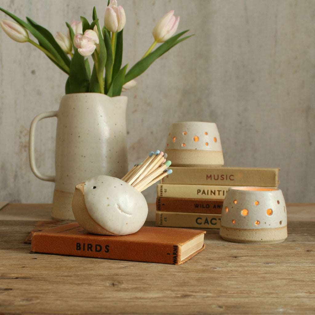 White bird match pot with stack of old books, lit tealight and vase of flowers