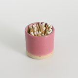 Pink ceramic match holder with matches on a light gray background