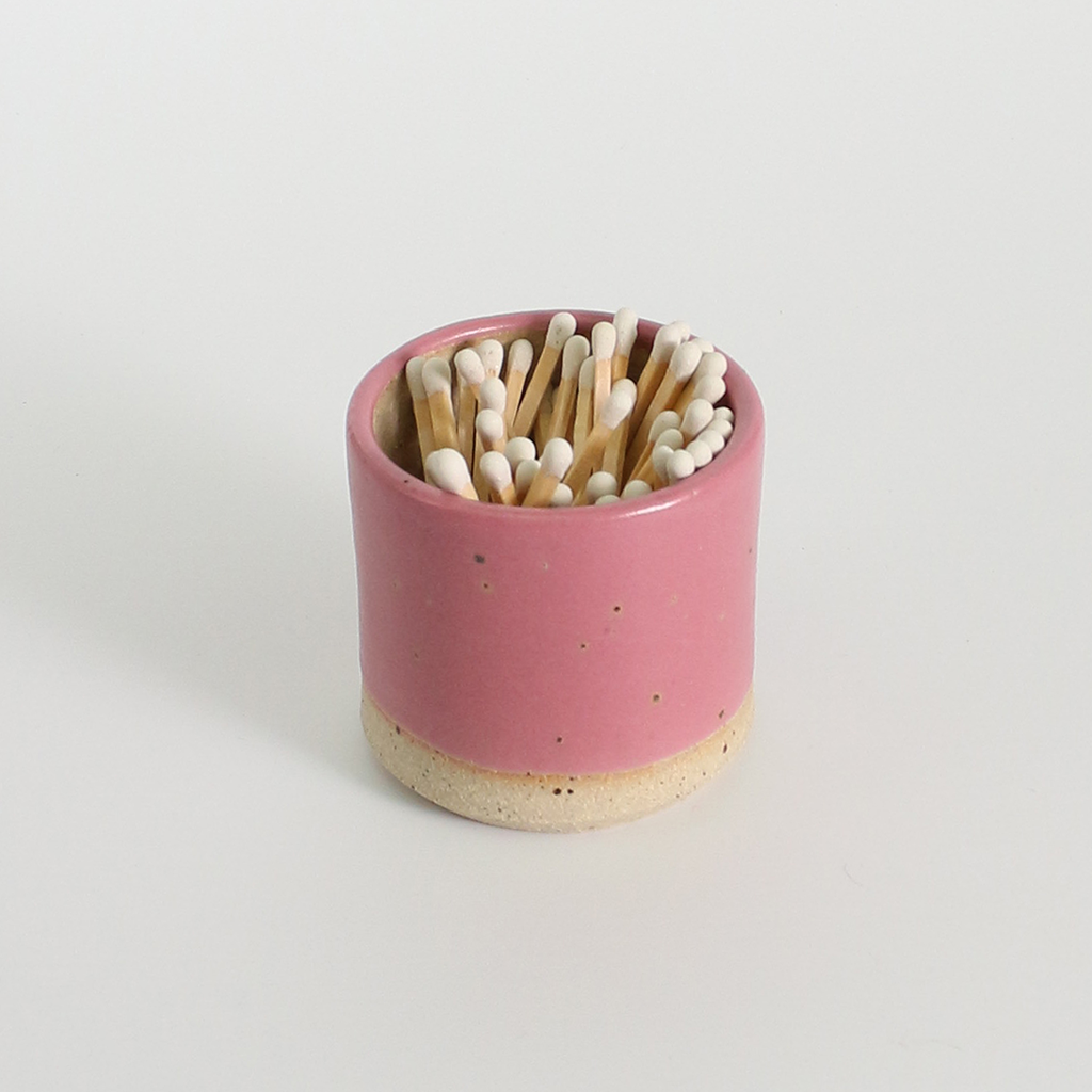 Pink ceramic match holder with matches on a light gray background
