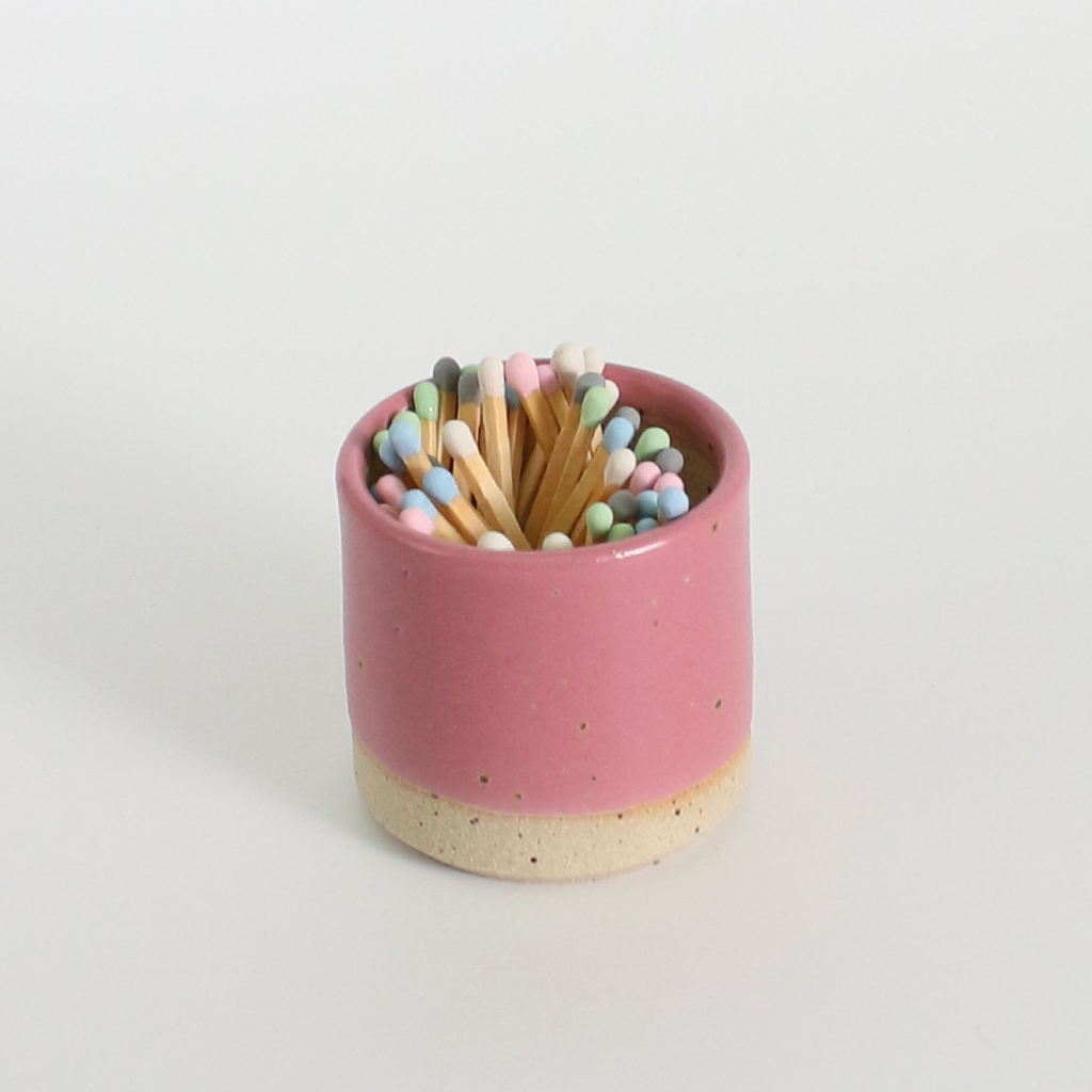 Pink ceramic match striker pot with multicoloured pastel wooden matches on a white background