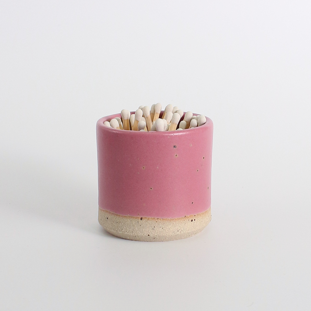 Pink ceramic match striker pot with wooden matches on a white background