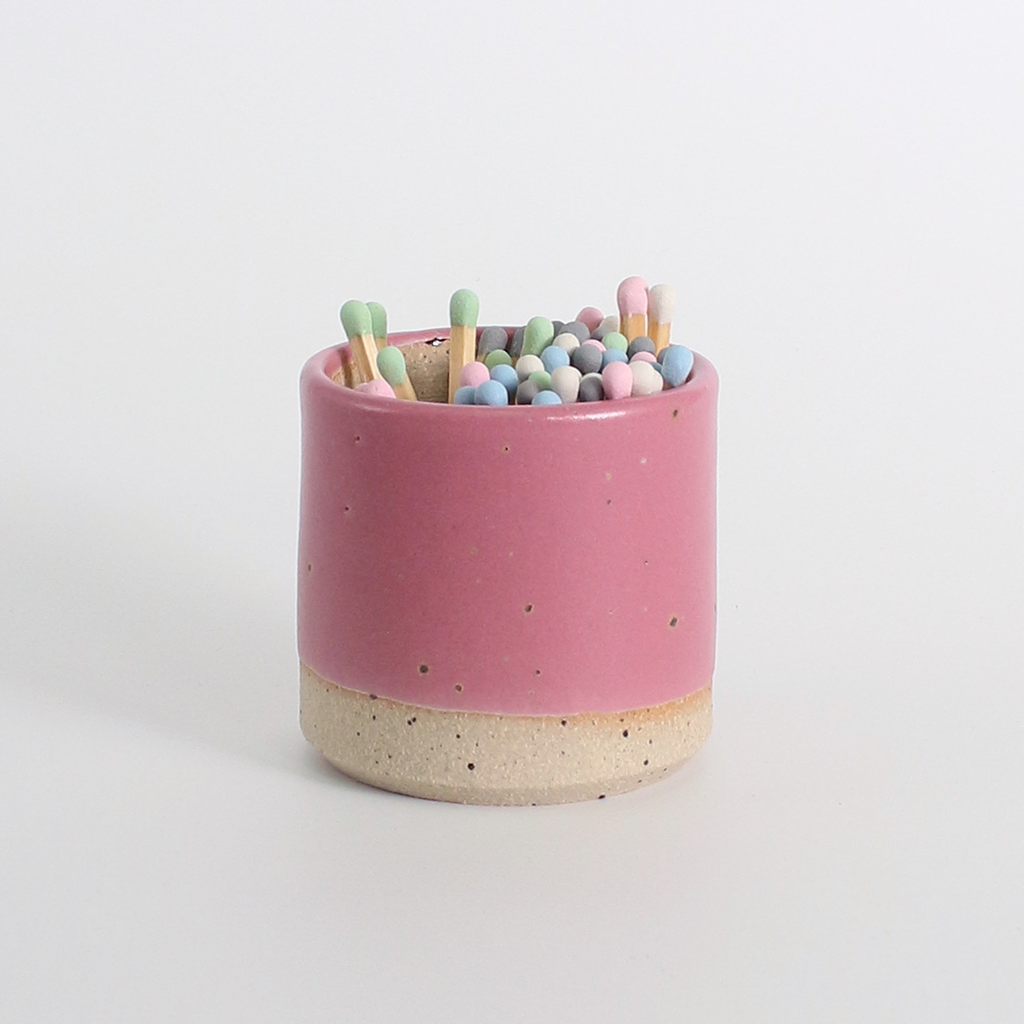 Pink ceramic match striker pot with multicoloured pastel wooden matches on a white background
