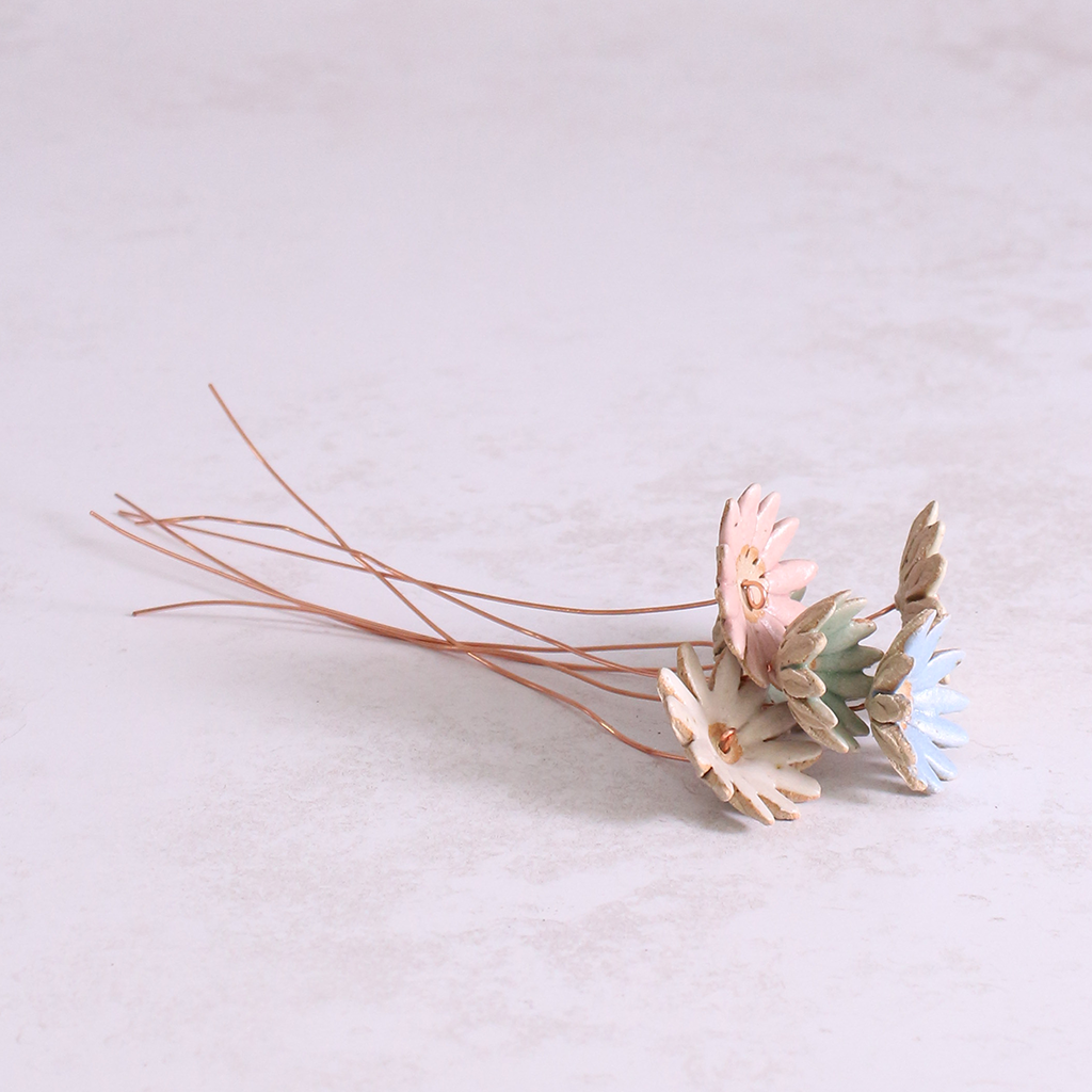 Several handmade ceramic daisy flower stems in different pastel glazes, creating a colourful ceramic bouquet.