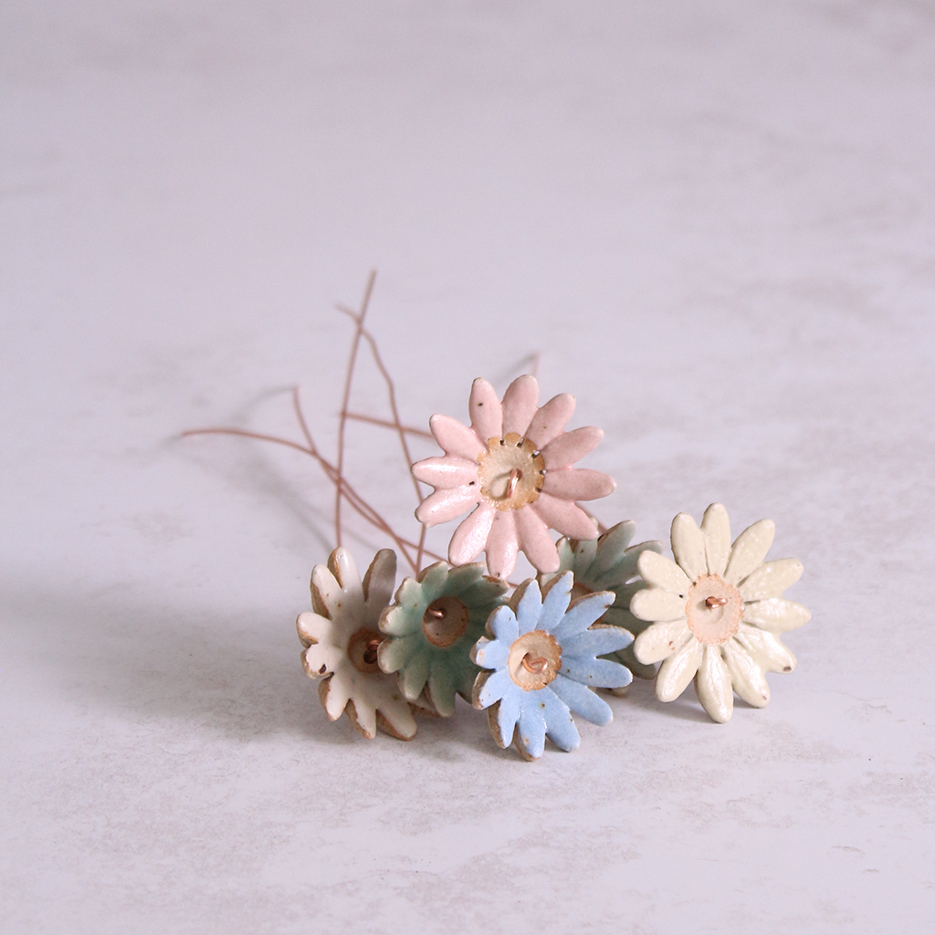 Several handmade ceramic daisy flower stems in different pastel glazes, creating a colourful ceramic bouquet.
